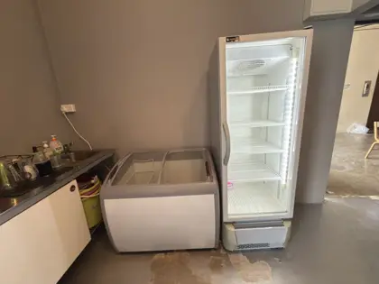 AANRS drink chiller rental Singapore, lit glass-door chiller and a sliding-lid chest freezer parked against a wall in a back-of-house area