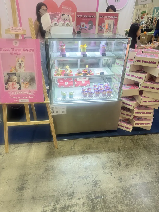 AANRS cake chiller rental Singapore, glass display of decorated pet treats beside stacks of pink boxes at an expo booth