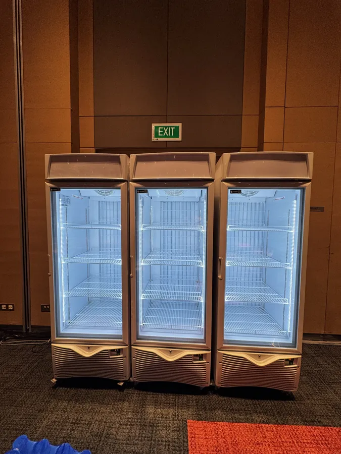 AANRS drink chiller rental Singapore, three empty glass-door chillers lined up against a timber wall in a carpeted function room