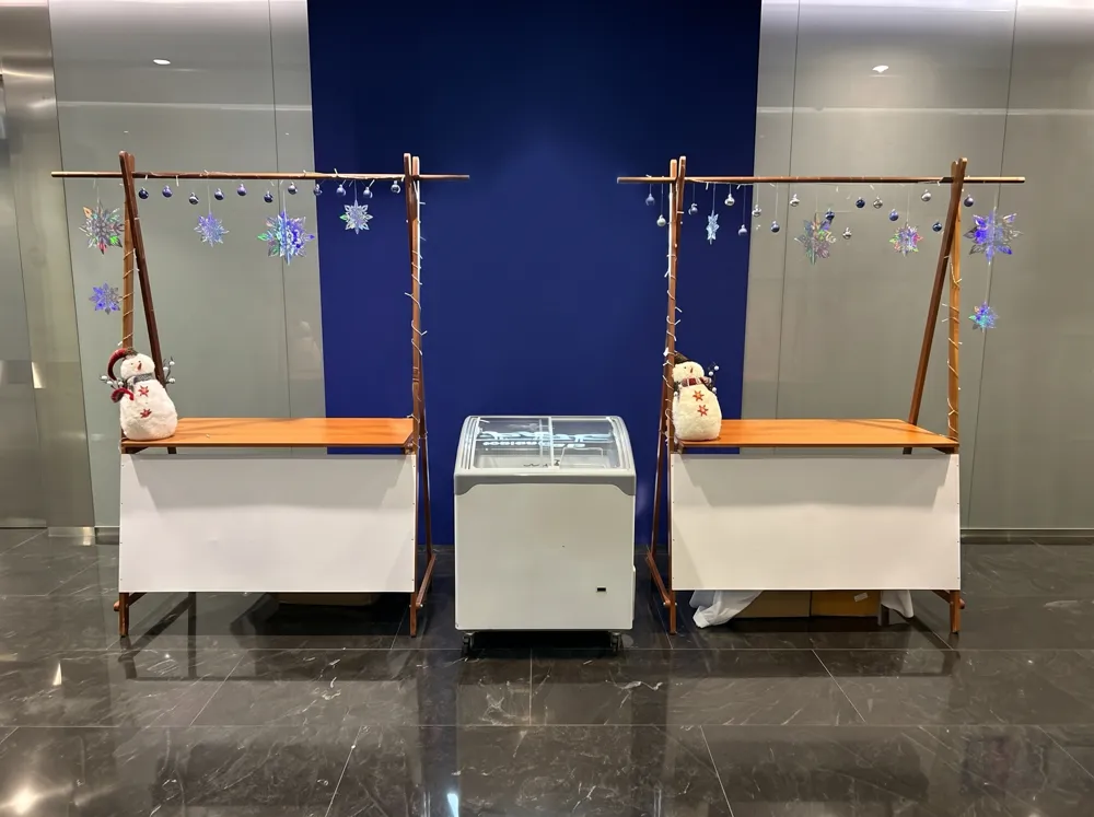AANRS glass chest freezer rental Singapore, curved sliding-lid freezer set between two timber stalls dressed with snowflakes and snowmen in a mall lobby